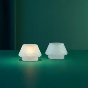 Gran lyslykter i frostet hvitt glass fra Hadeland Glassverk arrangert sammen med glasstrær i samme serie i et mørkt, elegant miljø.