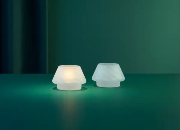 Gran lyslykter i frostet hvitt glass fra Hadeland Glassverk arrangert sammen med glasstrær i samme serie i et mørkt, elegant miljø.