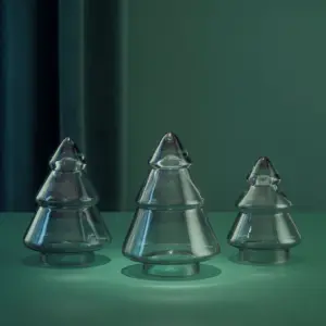 Tre røkgrå glasstrær fra Hadeland Glassverk plassert på grønn overflate med stemningsfull belysning.