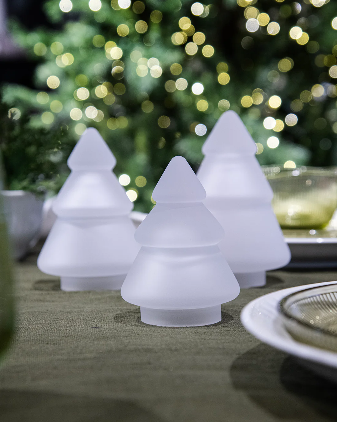 Hvite frostede glasstrær fra Hadeland Glassverk arrangert på grønn overflate i vinterlig belysning.