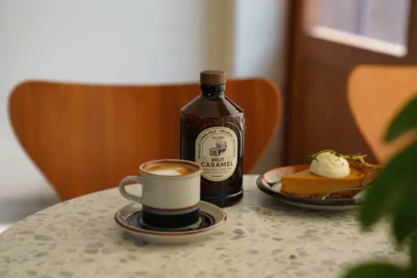 Kaffekopp og dessert står på et rundt steinbord sammen med en flaske Bacanha Brut Caramel.