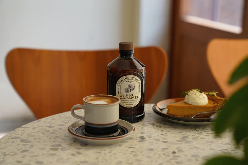 Kaffekopp og dessert står på et rundt steinbord sammen med en flaske Bacanha Brut Caramel.