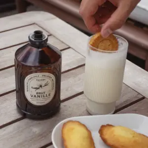En flaske Bacanha Brut Vanille står ved siden av et glass melk hvor en kjeks dyppes.