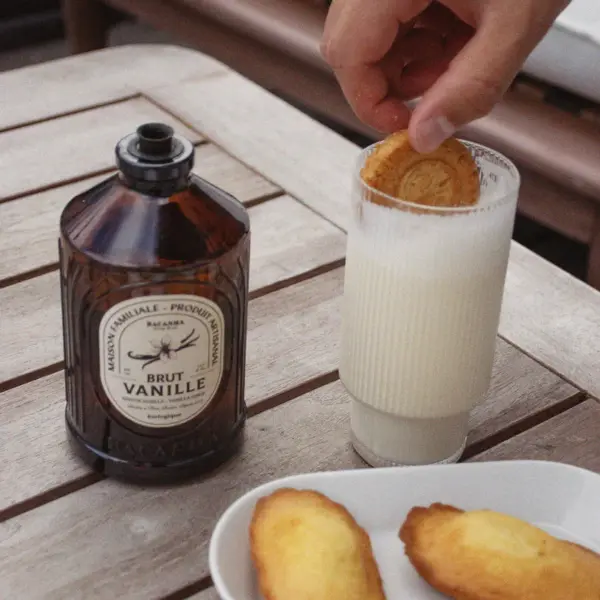 En flaske Bacanha Brut Vanille står ved siden av et glass melk hvor en kjeks dyppes.