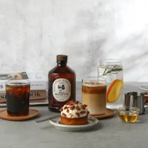 Bacanha Brut Noisette står på et bord sammen med iskaffe, latte, dessert med nøtter og et glass vann med sitrus.