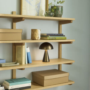 Mush oppladbar og dimbar bordlampe i Burnished Brass fra Hübsch plassert i en hylle, med varmt stemningslys og mykt uttrykk.