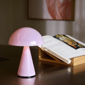 Mush oppladbar og dimbar bordlampe i Light Pink fra Hübsch plassert på et bord ved en bok, med mykt og stemningsfullt lys.